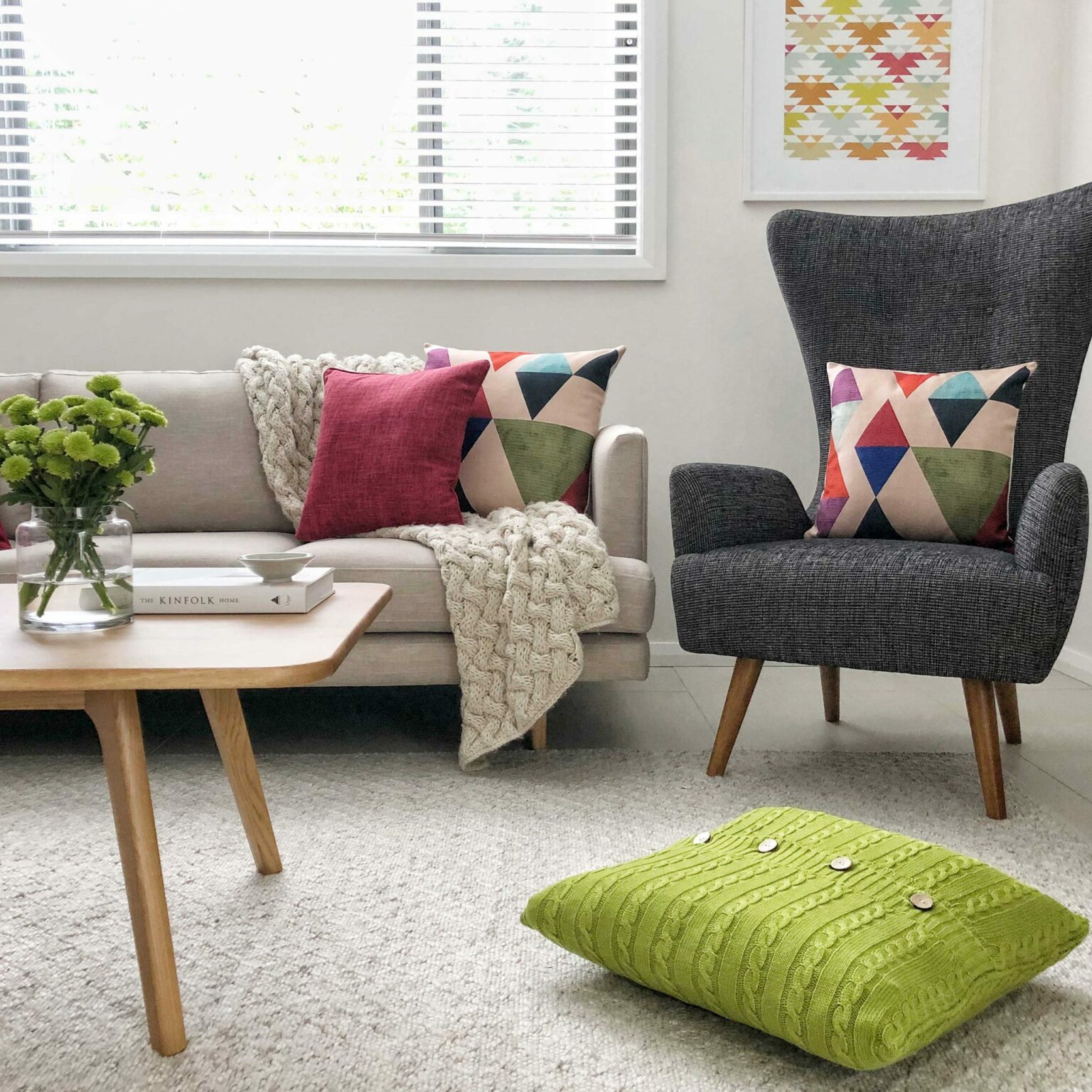 Living room with a grey chair and beige sofa with bright patterned cushions and a green floor knit cushion