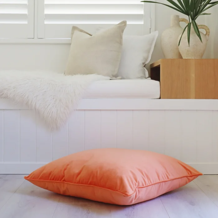 A large coral and peach floor cushion lays within a white room