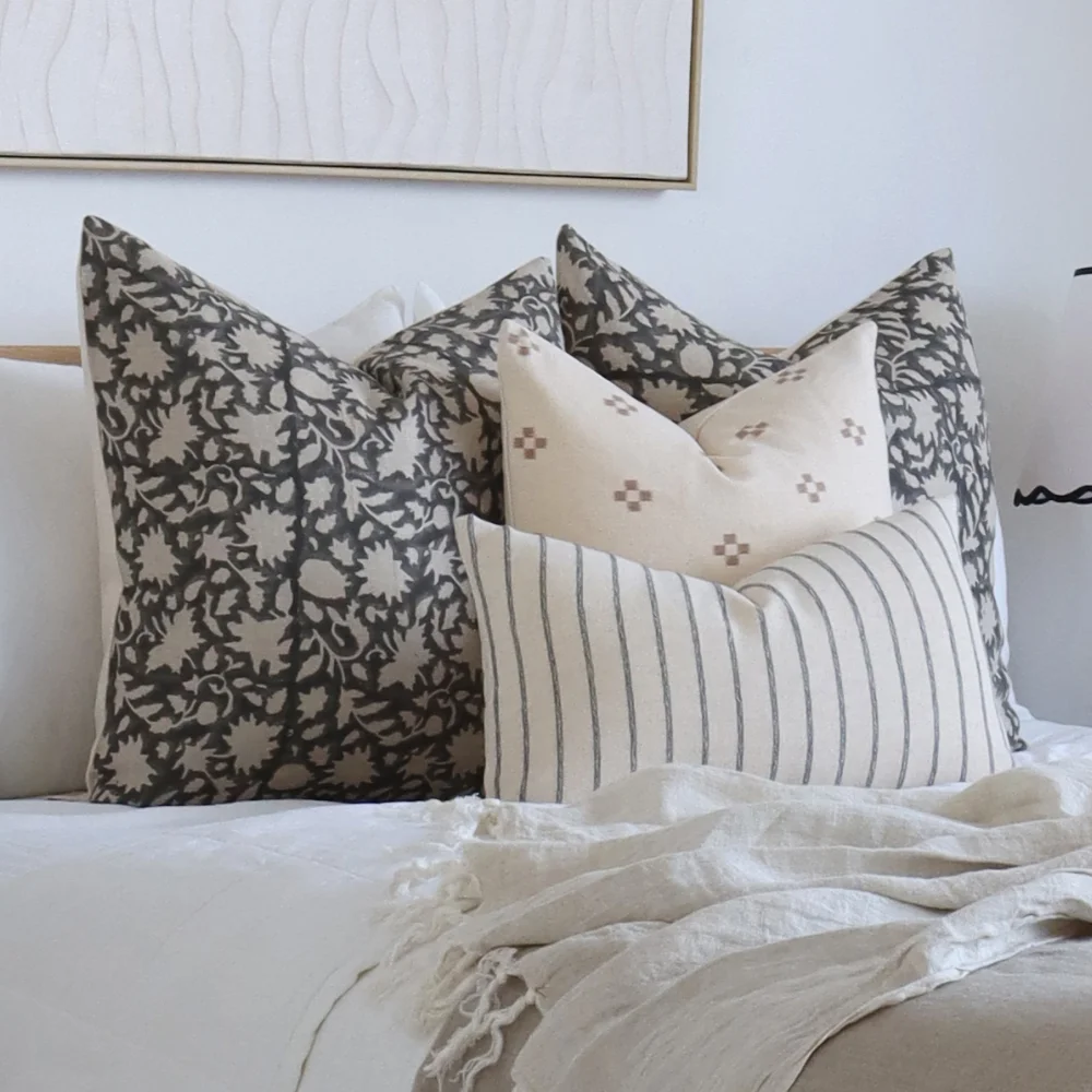 Some designer cushion sets on a light coloured bed in a room with lots of natural light.