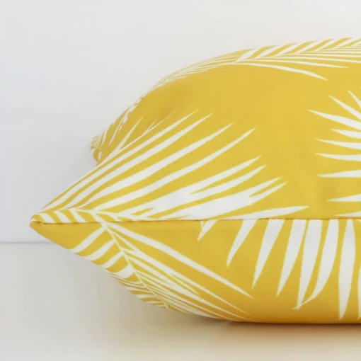 Side angle of a yellow palm printed cushion cover that has outdoor fabric and a square shape.