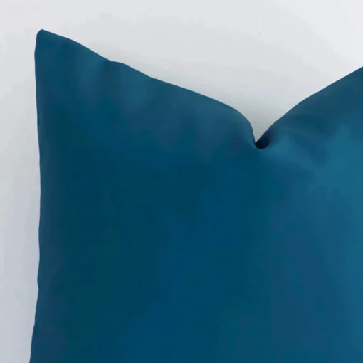 A macro image of the top left corner of this solid-coloured outdoor cushion. It is possible to see the finer detail of the square shape and teal colour.