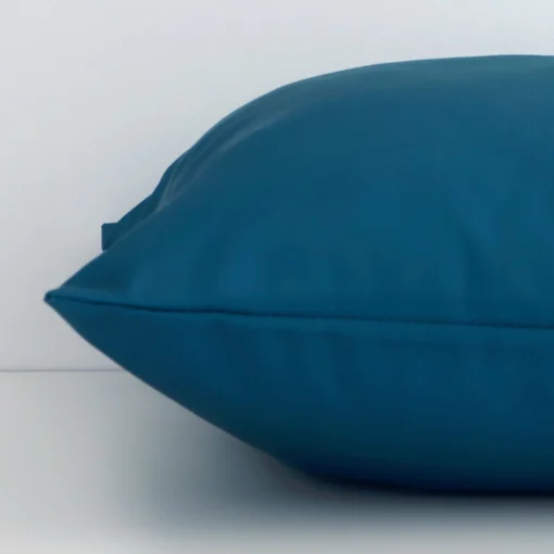 The edge of this outdoor square cushion in teal is shown. The shot shows the solid-coloured design and the front and rear panels.