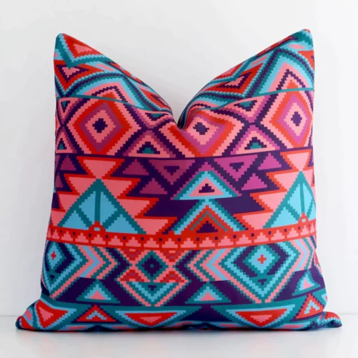 White wall with a geometric cushion laying against it. It has a distinctive outdoor fabric and has a square shape.