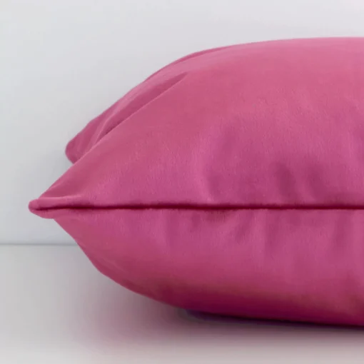 A solid-coloured blush cushion cover is laid flat. This angle shows the side of the velvet fabric and its square shape.