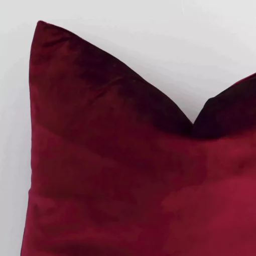 A very close image of the corner of a solid-coloured velvet cushion.The finer detail of the square shape and burgundy colour are visible.