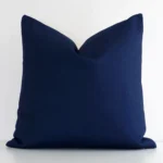 Dark blue linen cushion cover features prominently against a white wall. It is a square design and has a solid-coloured finish.