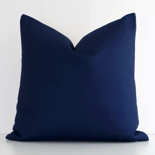 Dark blue linen cushion cover features prominently against a white wall. It is a square design and has a solid-coloured finish.