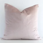 A lovely square dusty pink cushion cover arranged in front of a white wall. The solid-coloured style complements the velvet material.