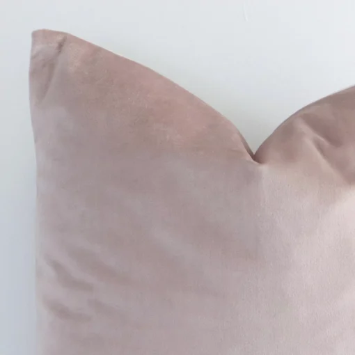 This image shows a dusty pink solid-coloured cushion cover from a very close range. The corner of its square shape and velvet material are more clearly shown.