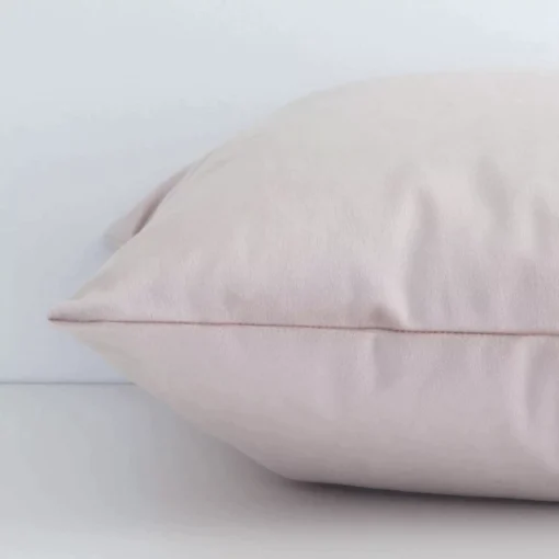 Lateral angle image of a velvet square cushion. The dusty pink colour and solid-coloured design are highlighted along its seams.