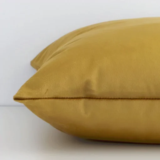 A velvet gold mustard cushion cover shown laying on its side. The solid-coloured design and its square shape are shown side on.