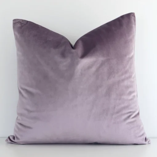 A velvet square cushion cover that has a solid colour design is shown vertically against a white wall. It has a wonderful lavender colour.