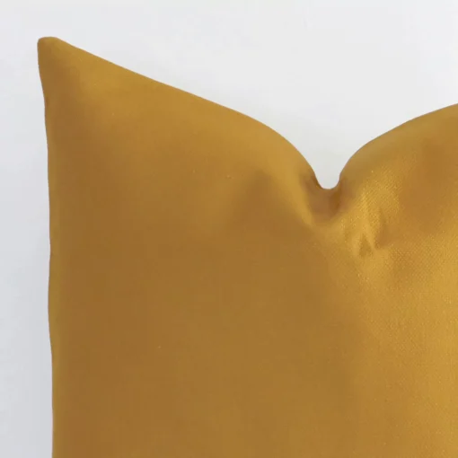 A mustard linen cushion cover’s corner is shown in more detail. It is possible to see the square design and solid-coloured finish in much more detail.