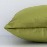 Olive green solid coloured cushion cover laying sideways against white wall. The rectangle size and velvet material are shown highlighting the seams.