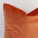 Cropped shot of top left corner of this solid-coloured orange cushion cover. This viewpoint shows the velvet fabric and square shape with more precision.