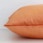 Bold orange cushion laid horizontally. This perspective shows the edge of the velvet fabric and its square shape.