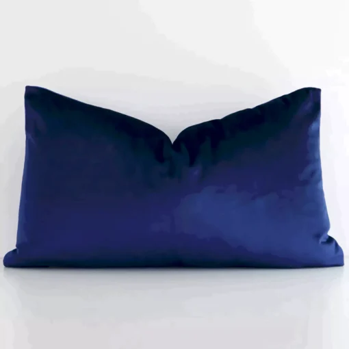 Royal blue cushion cover in front of a white wall. It has a rectangle size and is made from a velvet material.