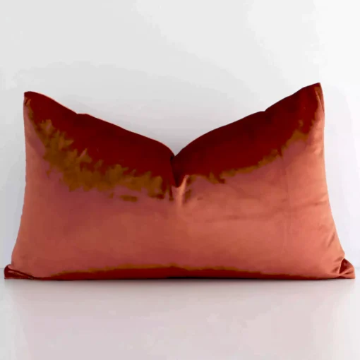 Bold rectangle rust cushion positioned in front of white wall. It has an elegant velvet material.