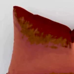 Close range image of rust cushion. The rectangle size and velvet material can be seen in detail.