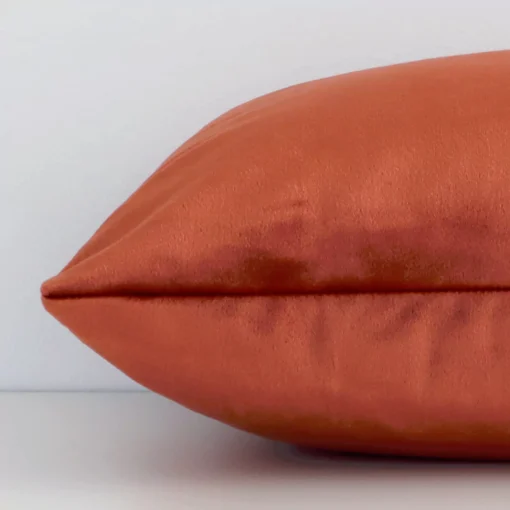 Side angle shot of velvet rectangle cushion cover. The rust hue is shown along its seams.