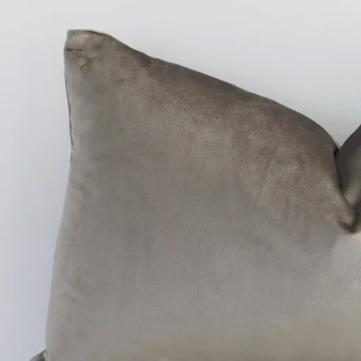 Enlarged shot of the corner of this rectangle solid colur cushion cover in taupe colour is shown against a brick wall. The image shows the quality and craftsmanship of the velvet material.