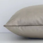 A taupe solid-coloured cushion arranged sideways in front of a wall. The rectangle shape and velvet fabric are shown and the seams are clearly visible.