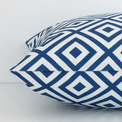 Enlarged image of the side of this blue outdoor cushion. The angle highlights how the square design and geometric decorative finish are joined along the seam.