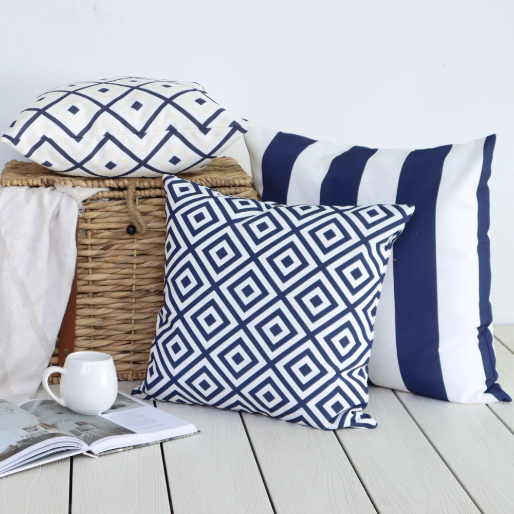 Three square outdoor cushions are arranged against a white wall and on top of a basket with a book in the foreground.