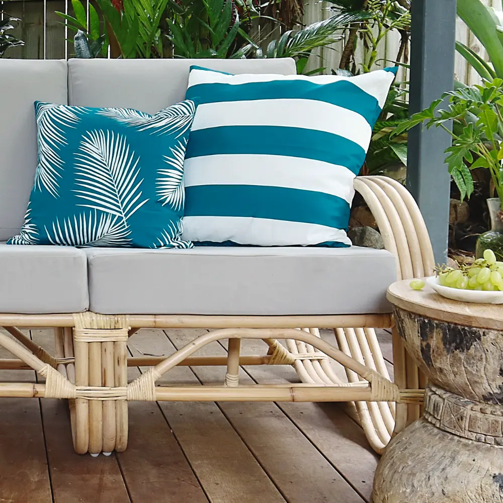 Two teal cushions arranged on a light grey and cane outdoor setting.